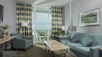 A living room with a sofa, a coffee table, a chair, and a balcony with curtains.