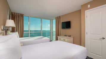 Quarto de hotel com duas camas, televisão, cômoda e uma grande janela com vista para o mar.