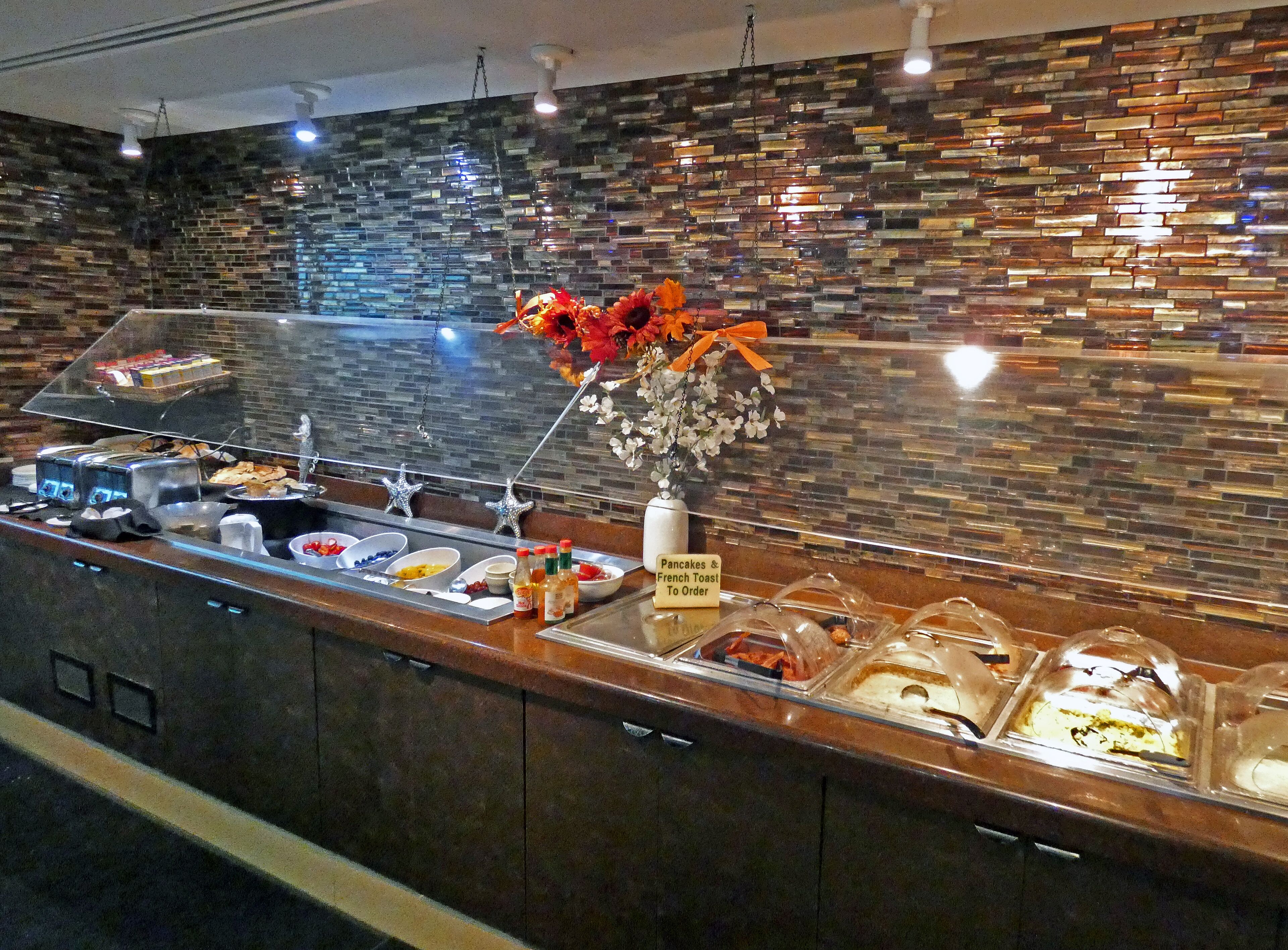 Un buffet de petit-déjeuner proposant divers plats, avec un panneau indiquant que des crêpes et du pain perdu sont disponibles.
