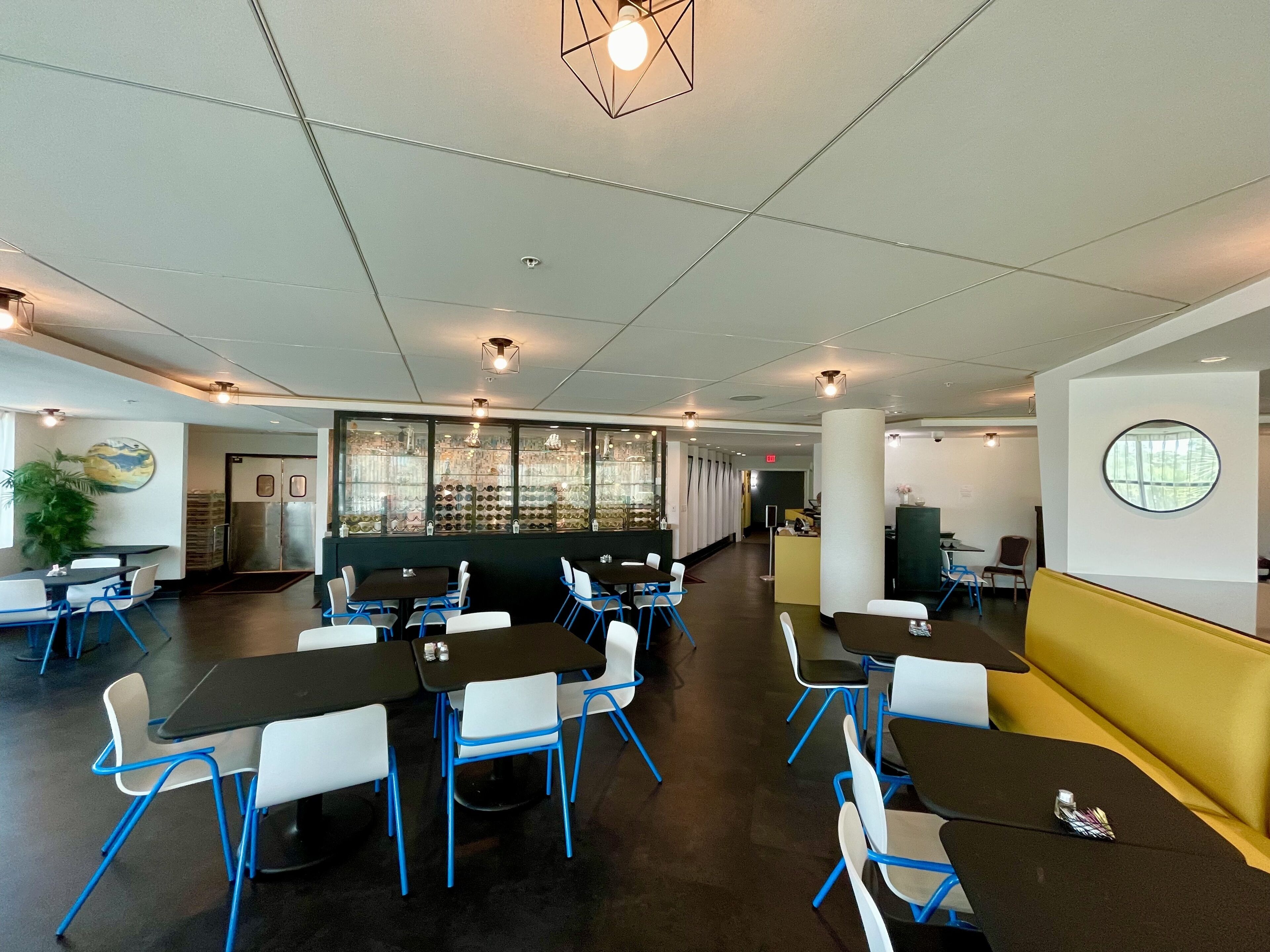 A modern dining area with black and white tables, blue chairs, and a yellow booth.
