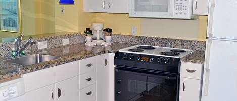 Une cuisine avec des armoires blanches, un comptoir en granit, un four à micro-ondes encastré, une cuisinière, un four et un évier.