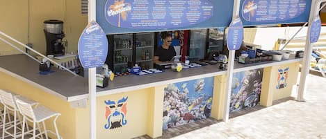 A beachside bar with a menu board, bar stools, and a mural of fish.