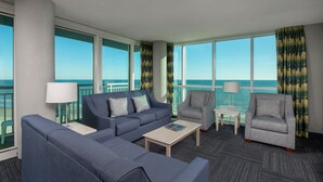 A modern hotel room with a large balcony, a sofa, a chair, a small table, and a lamp. - Avista Resort (North Myrtle Beach)