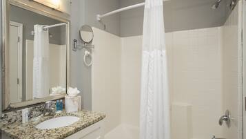 A bathroom with a sink, mirror, and shower area.