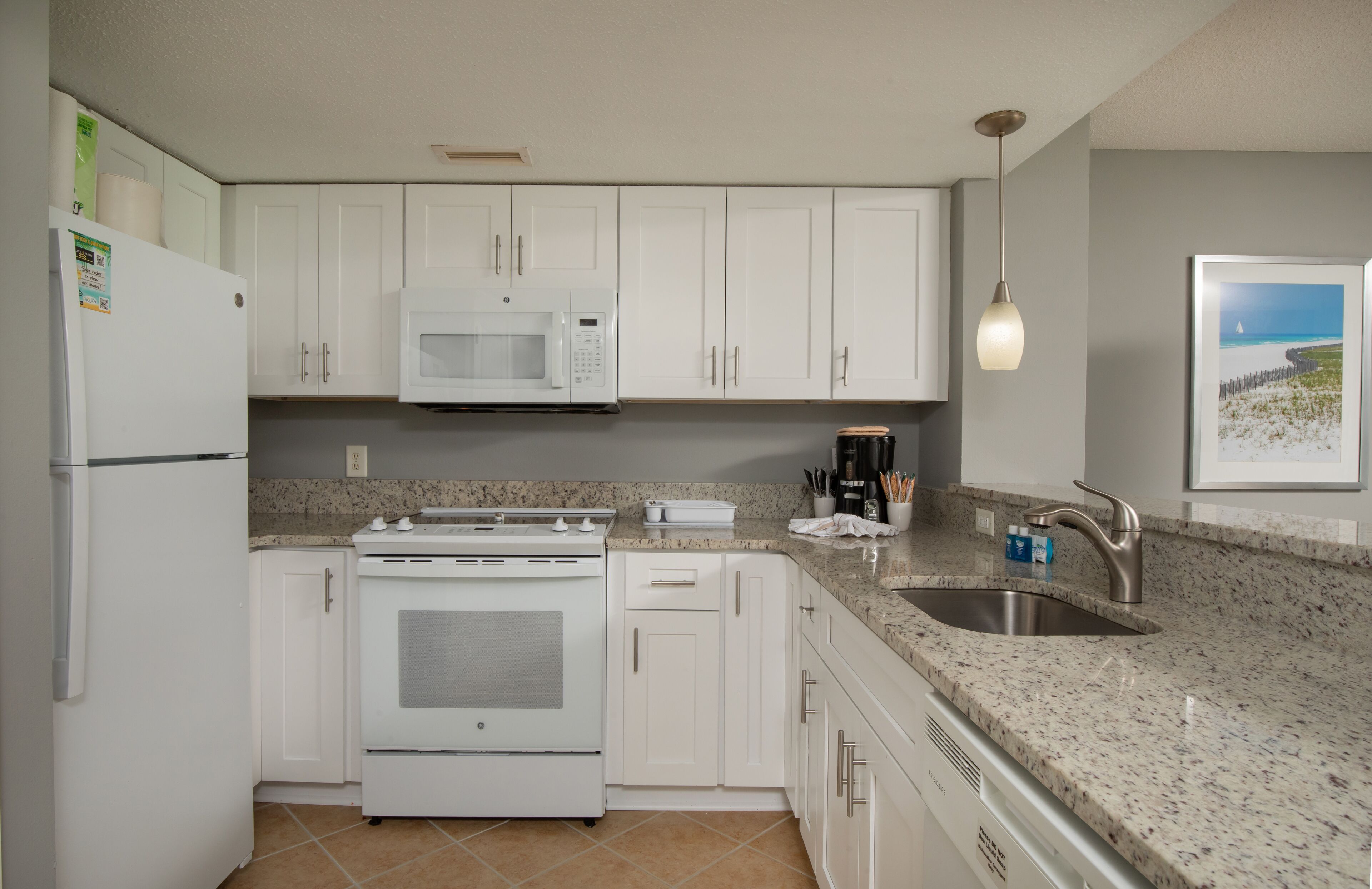 A kitchen with white cabinets, a microwave, stove, and a sink.