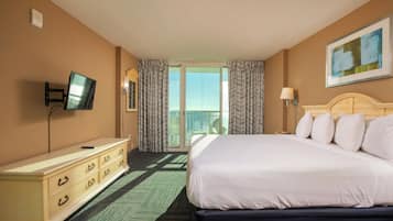 A hotel room with a bed, a dresser, a television, a balcony with curtains, and a painting on the wall.