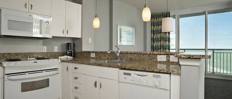 A modern kitchen with white cabinets, a granite countertop, a built-in microwave, a stove, a dishwasher, and pendant lights.