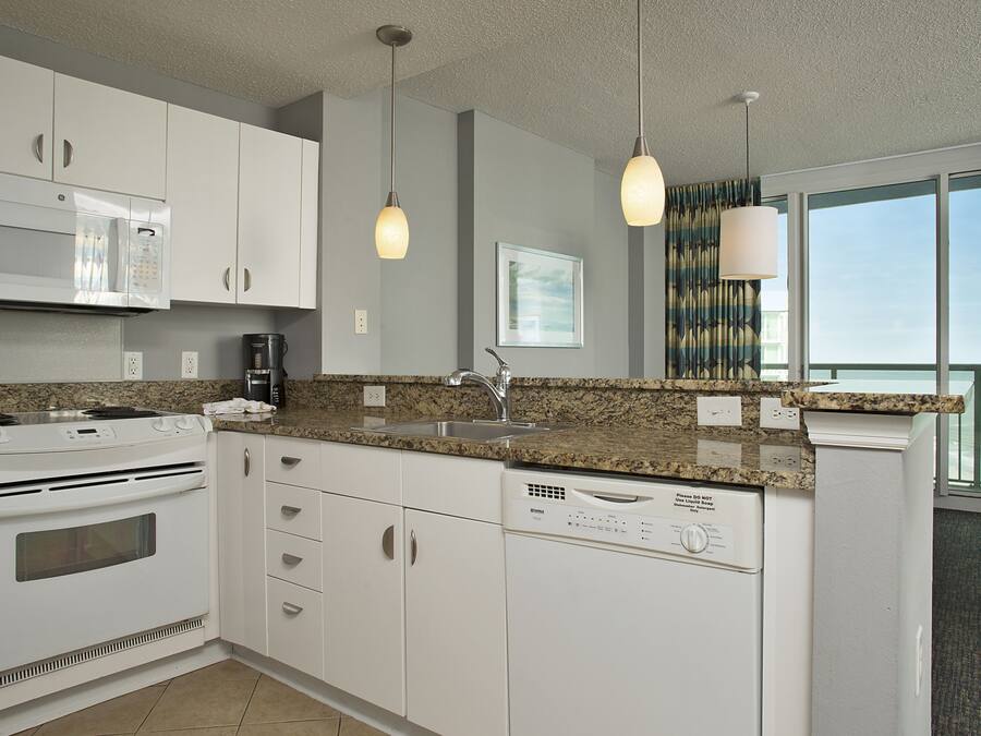 A modern kitchen with white cabinets, a granite countertop, a built-in microwave, a stove, a dishwasher, and pendant lights.