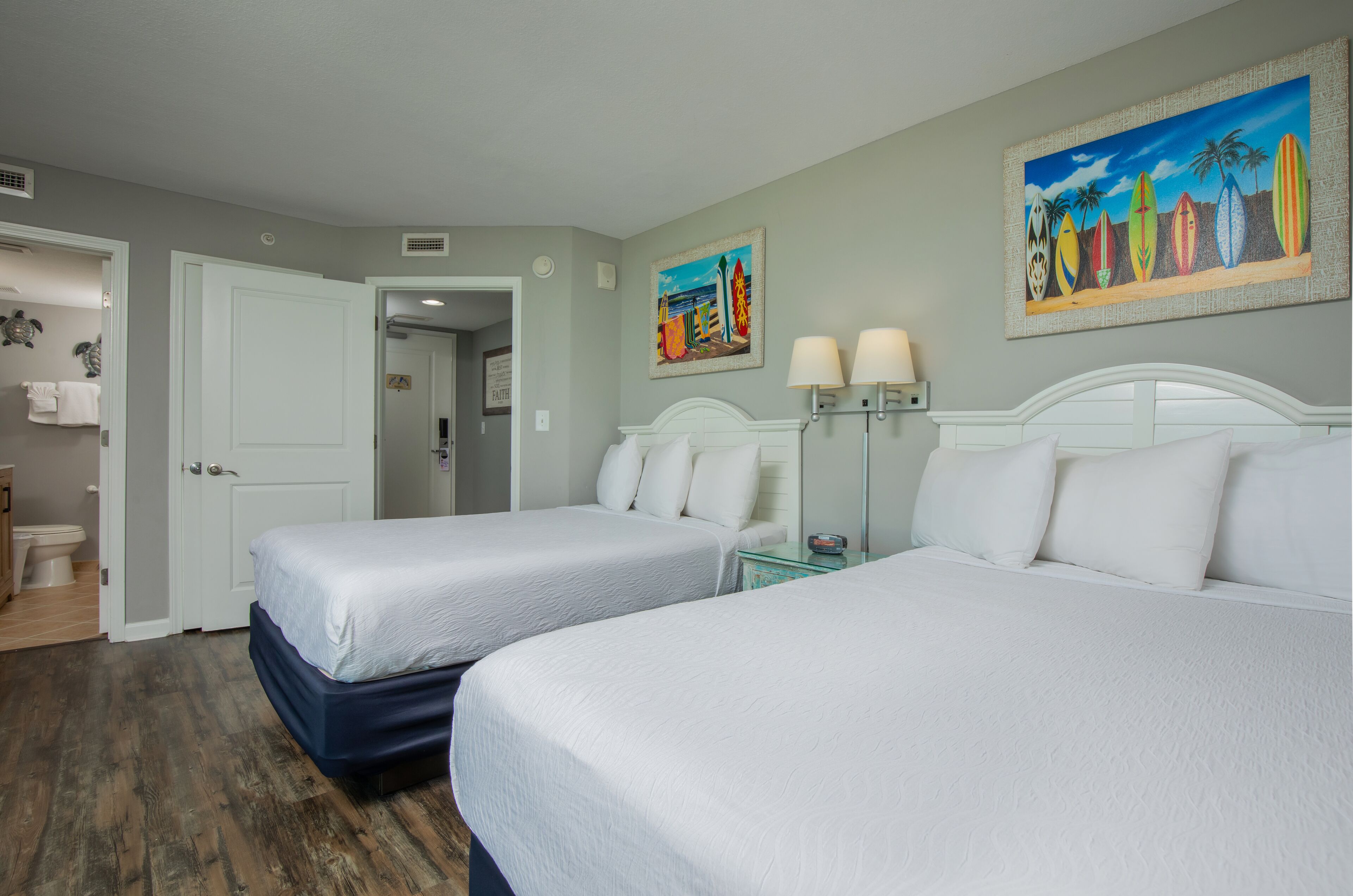 A hotel room with two beds, a bathroom, and a hallway.