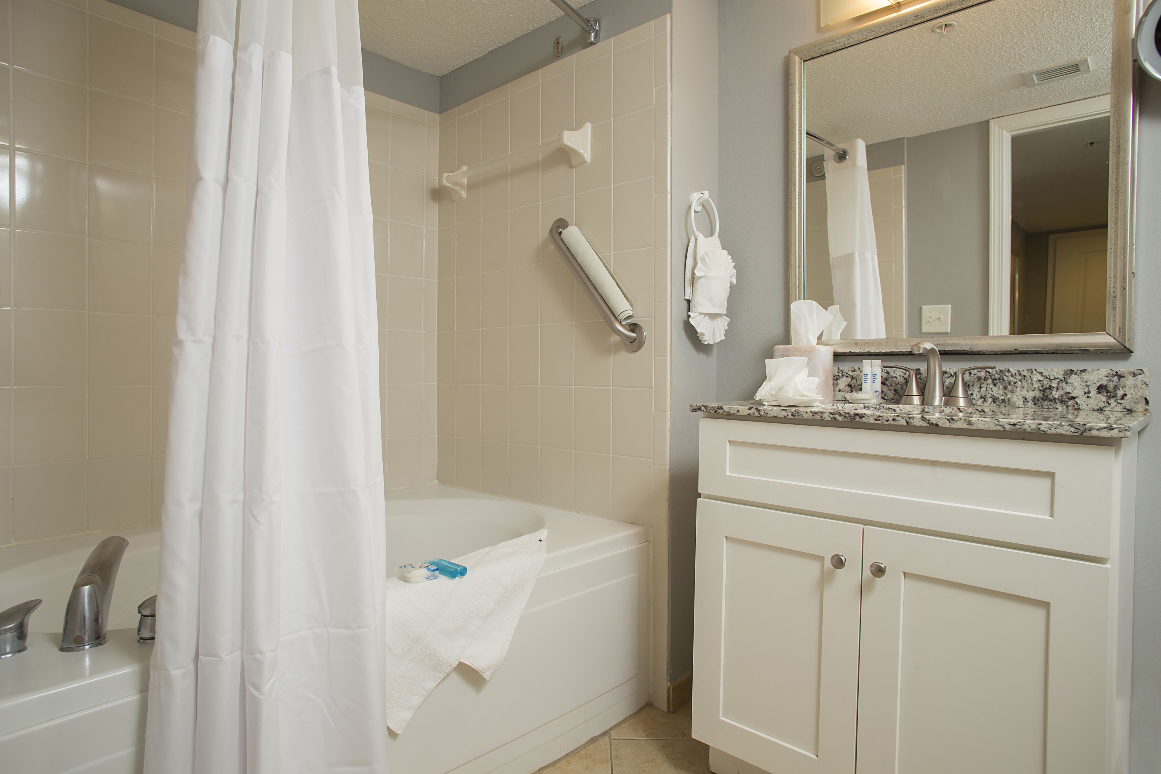 A bathroom with a bathtub, a shower curtain, a towel rack, a toilet, and a sink with a mirror above it.