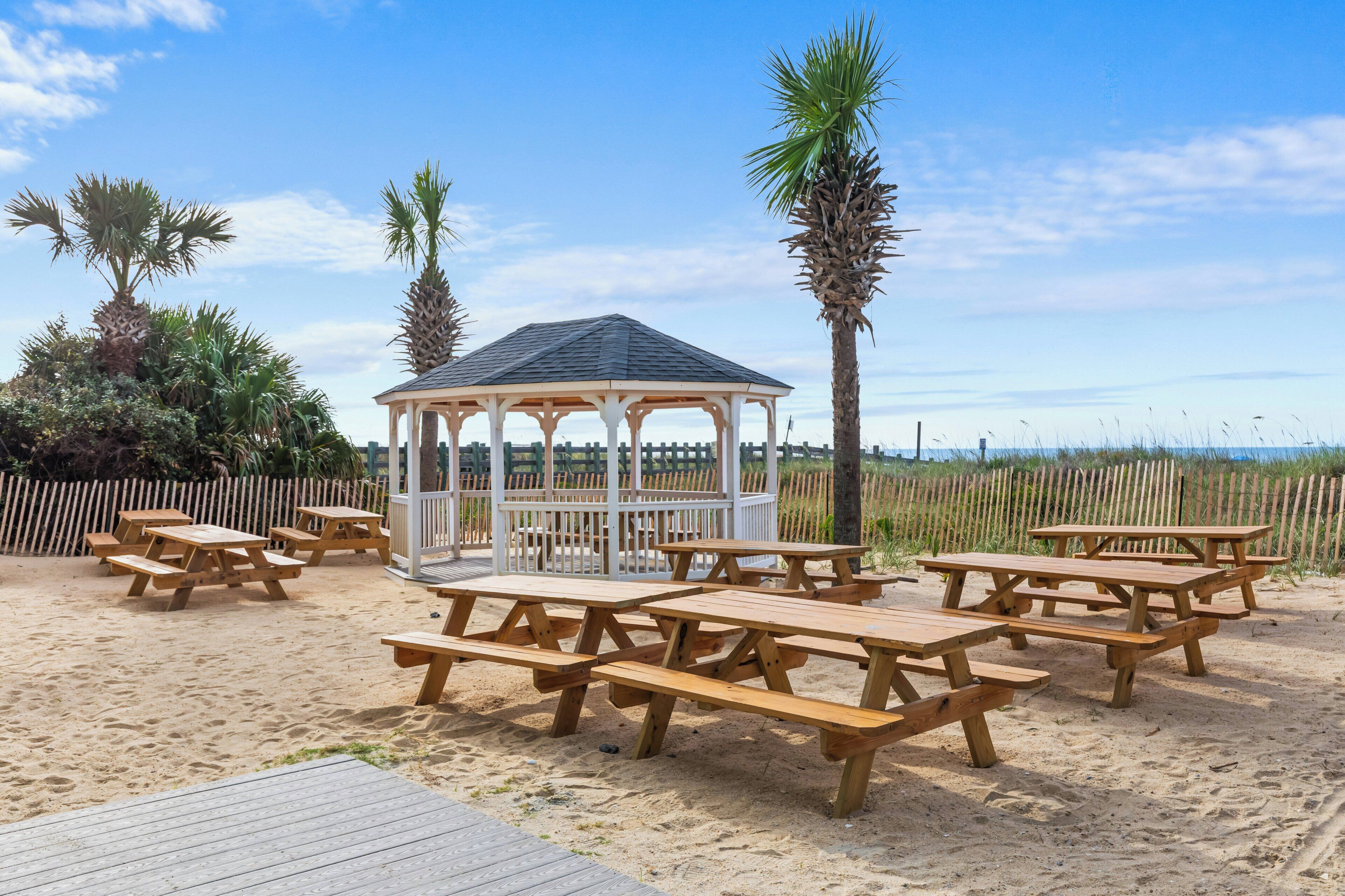 A beachside gazebo with picnic tables and palm trees.