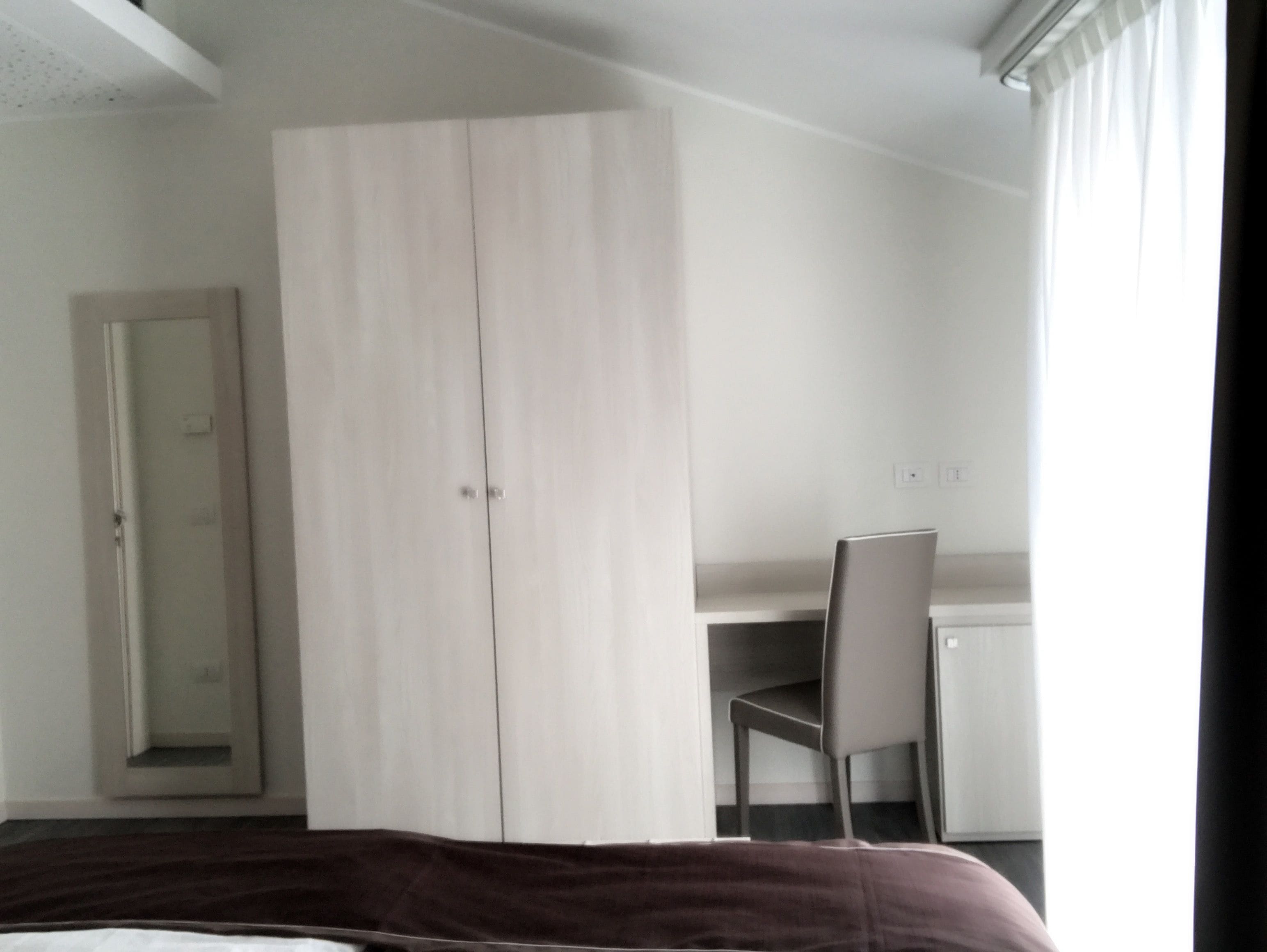 A bedroom with a bed, a wardrobe, a desk, and a chair.