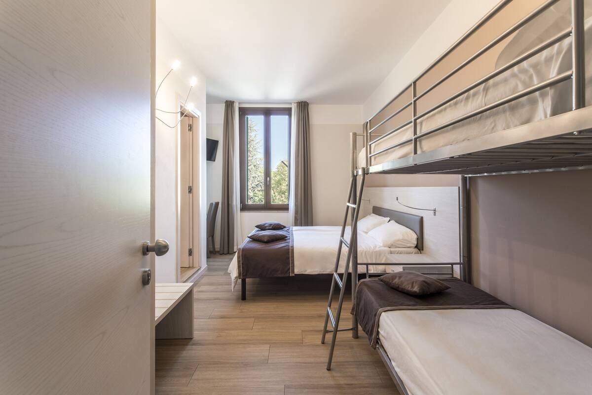 Ein kleines Hotelzimmer mit Stockbetten, einem Schreibtisch und einem Fenster mit Vorhängen.
