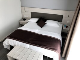 Habitación de hotel con una cama bien hecha, una mesita de noche y una pequeña mesa al pie de la cama.