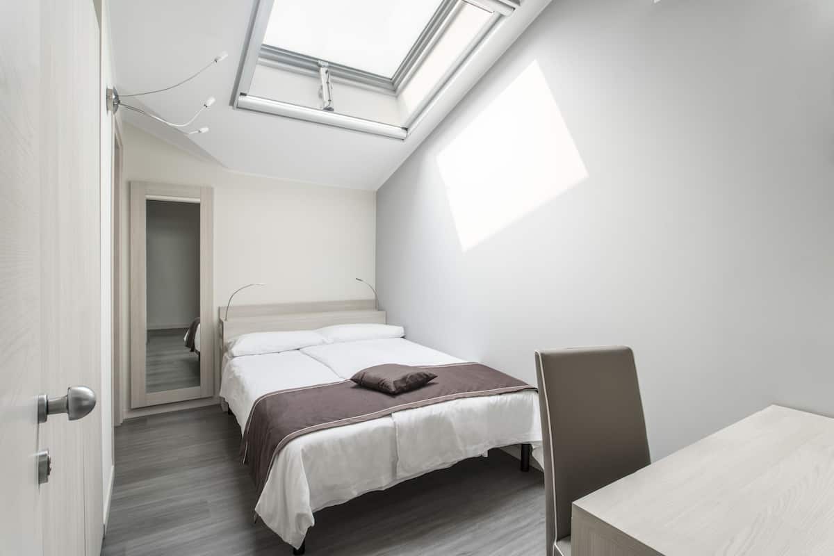 Ein modernes Schlafzimmer mit Dachfenster, einem Bett mit brauner Kopfteil, einem Nachttisch und einem Sessel.