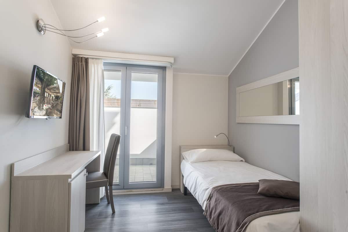 Ein modernes Schlafzimmer mit Schreibtisch, Stuhl, Bett und einem großen Fenster.