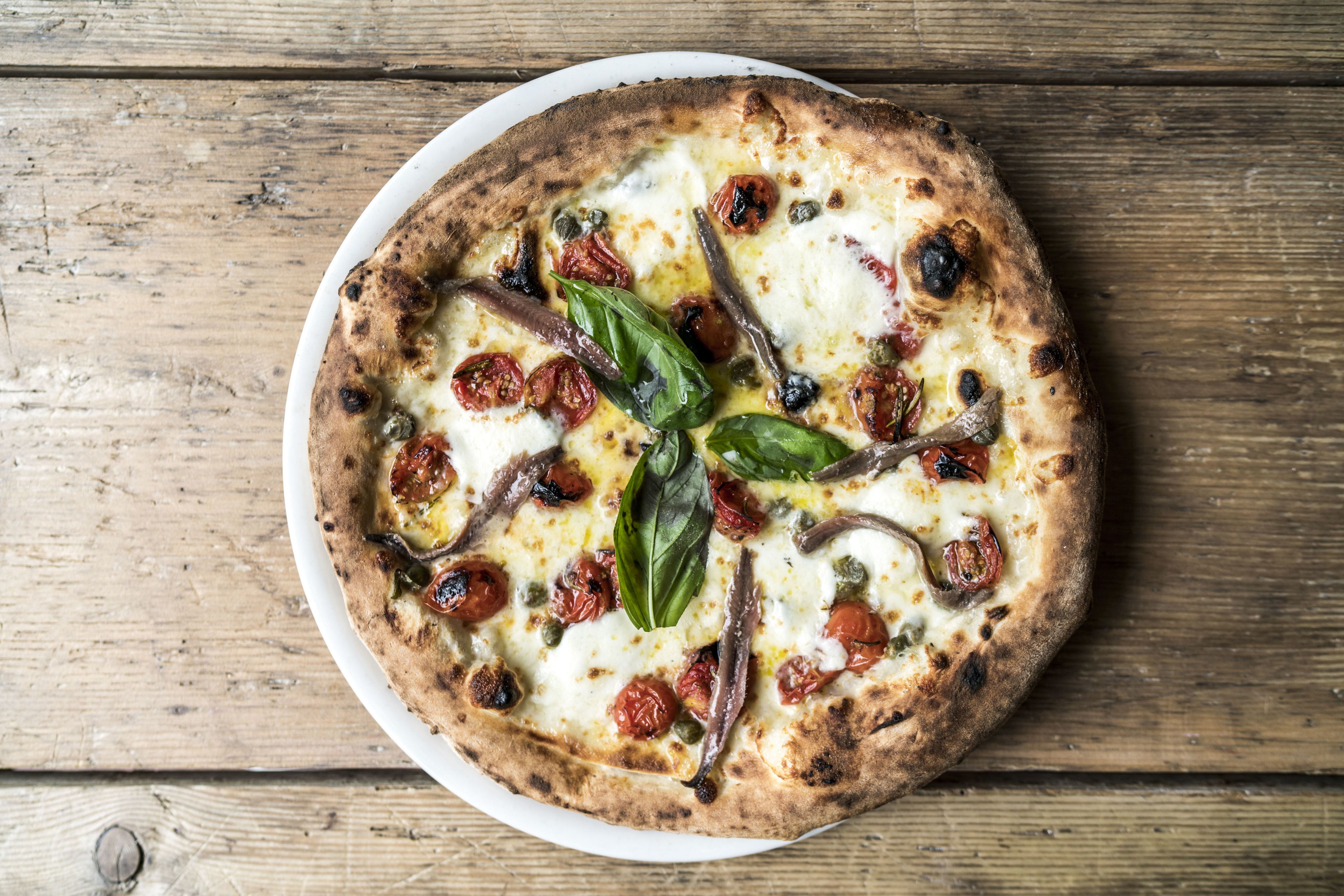 A pizza on a white plate with a rustic wooden background.
