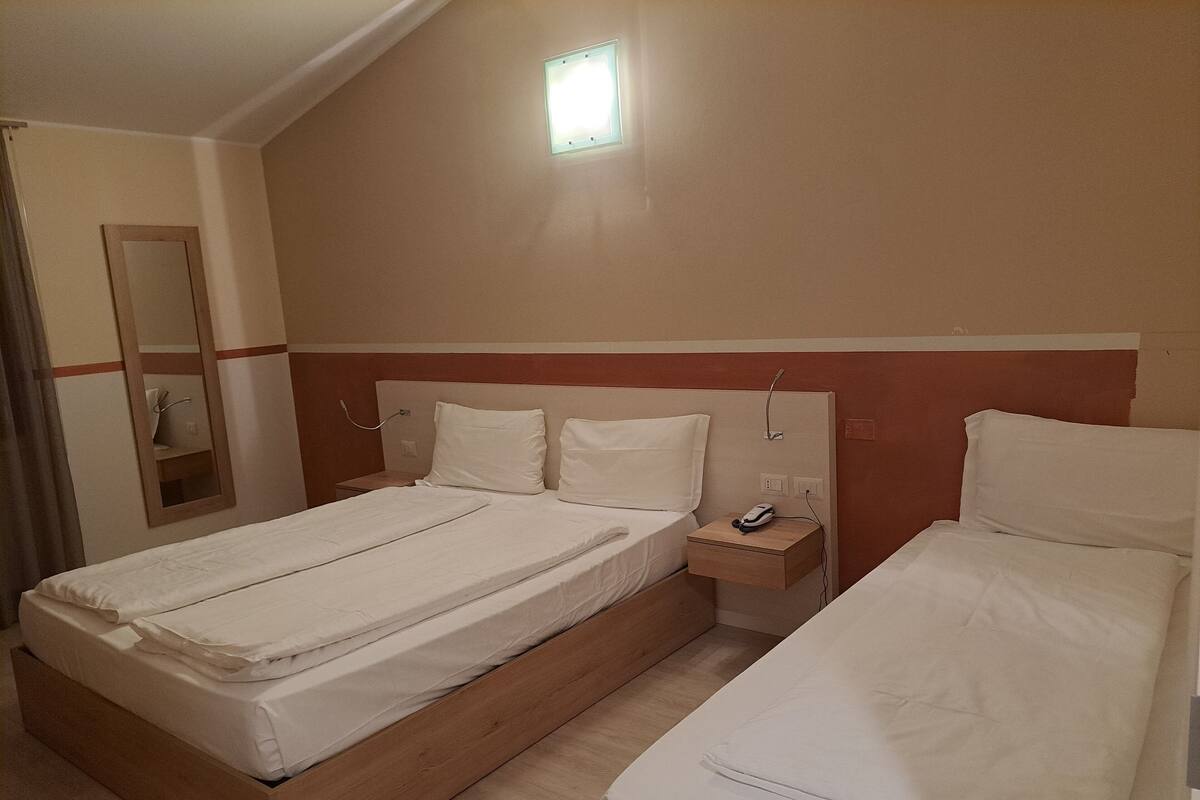 Ein Hotelzimmer mit einem Einzelbett, einem Nachttisch, einem Spiegel und einem Fenster.