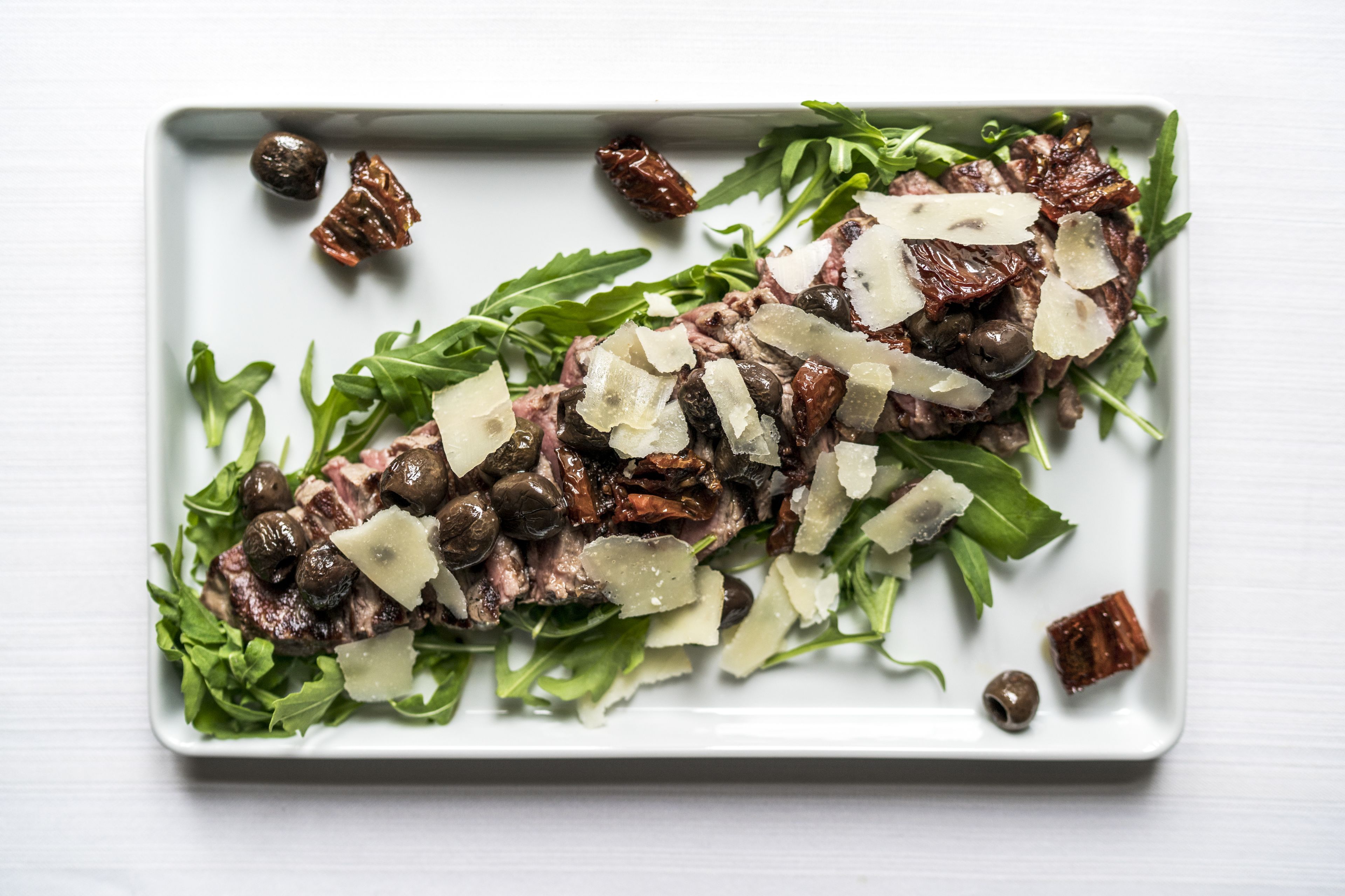 A rectangular white plate with a salad consisting of arugula, mushrooms, and shaved cheese.