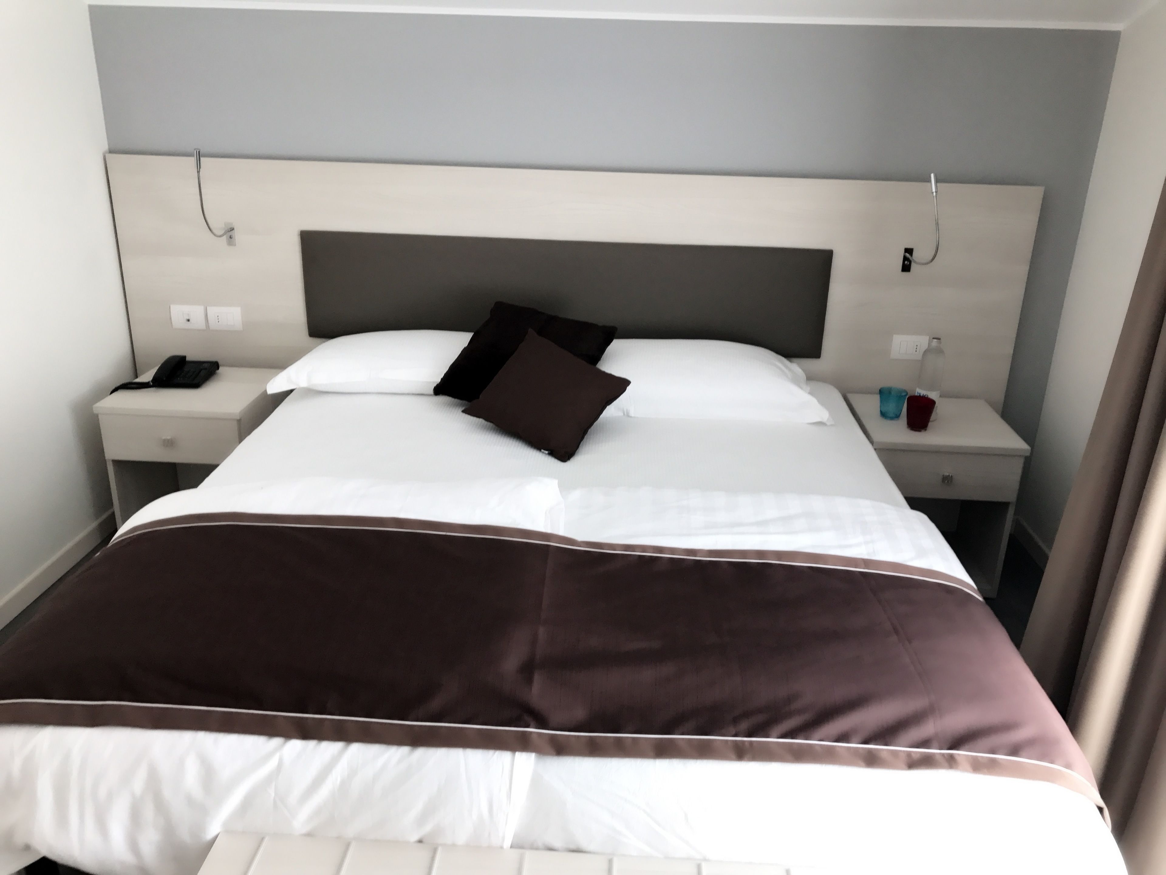 A hotel room with a large bed, two bedside tables, a headboard, and a nightstand with a phone and a cup.