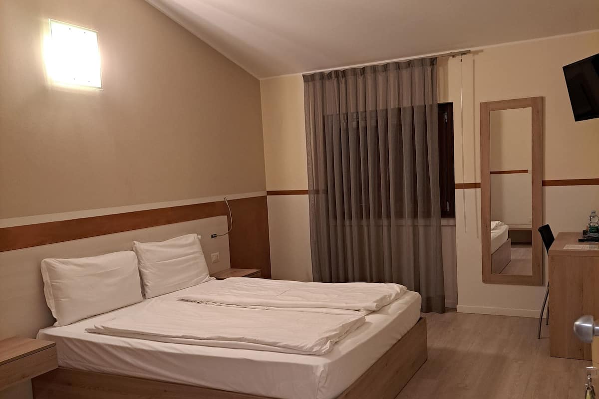 Ein Hotelzimmer mit einem großen Bett, einem hölzernen Kopfteil, einem Nachttisch, einem Schreibtisch mit Stuhl, einem Spiegel und einem an der Wand montierten Fernseher.