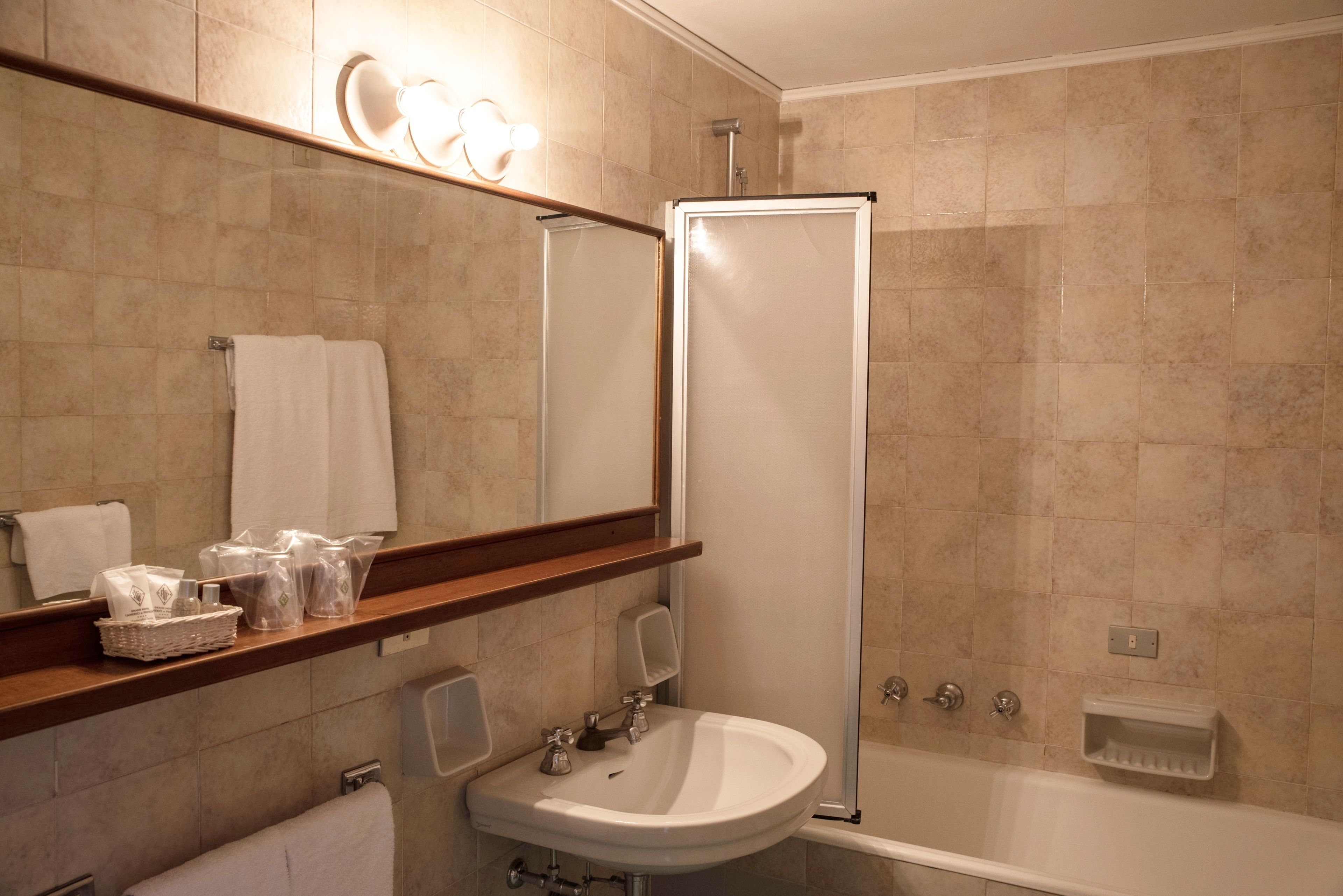 A bathroom with a sink, mirror, towel rack, shower, and a shelf with toiletries.