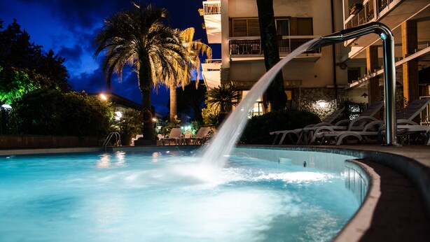 A swimming pool with a water fountain, lounge chairs, and a palm tree. - Grand Hotel Terme Tamerici e Principe (Montecatini Terme)