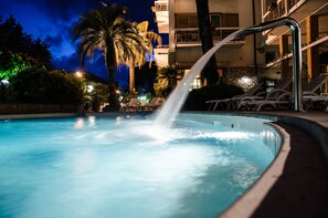 Une piscine avec une fontaine, des chaises longues et un palmier.