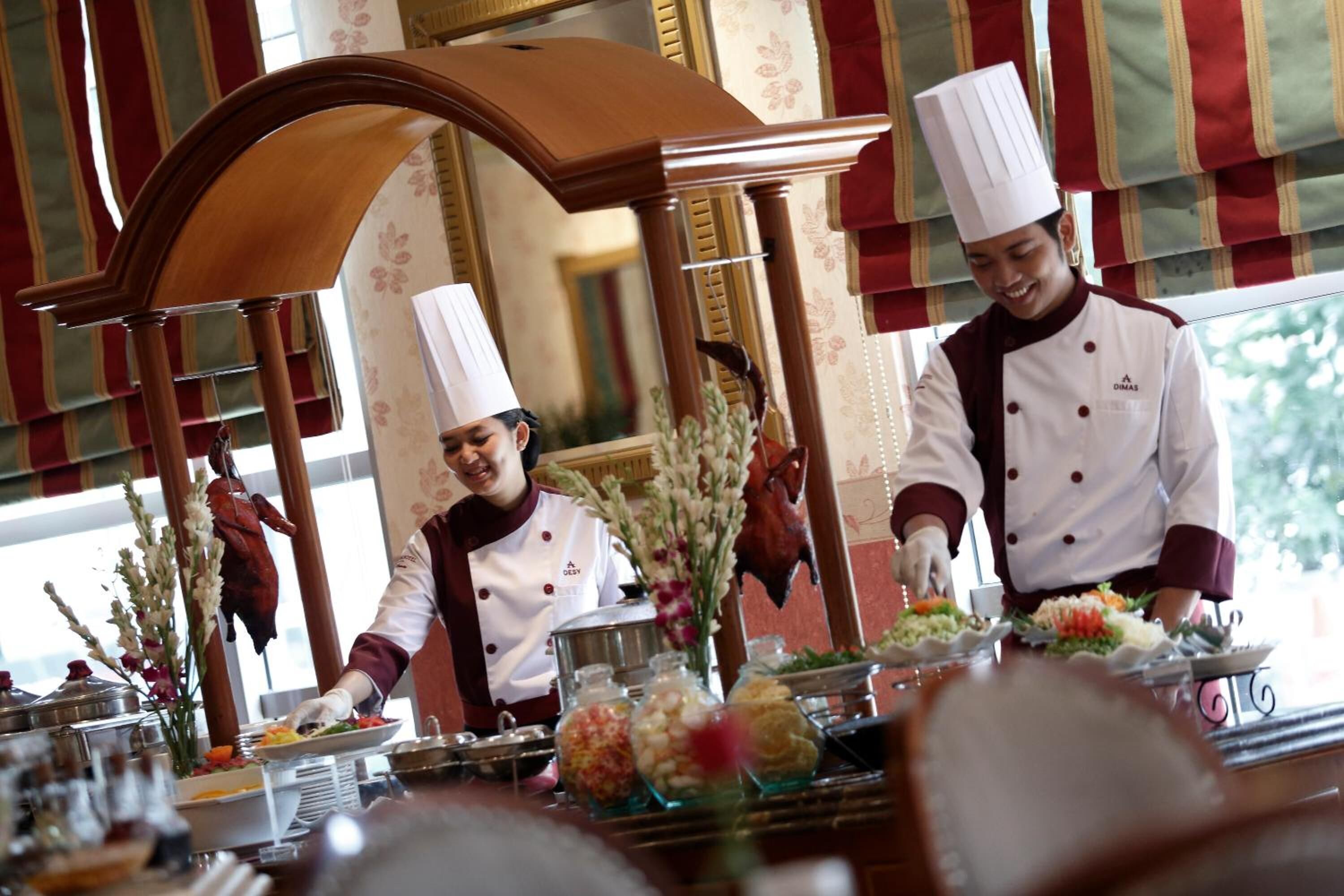 A professional kitchen with chefs preparing food, a buffet setup, and a decorative archway.