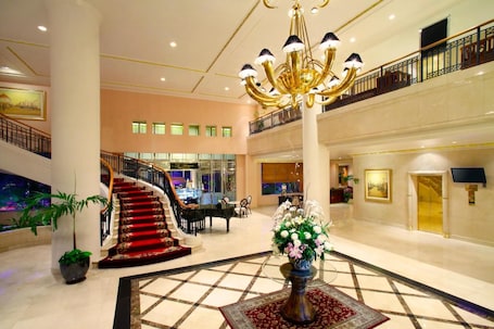 A spacious lobby with a grand chandelier, a piano, and a staircase leading to an upper level.