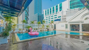 Una piscina con un flotador de flamenco rosa, rodeada de plantas en macetas y edificios modernos.