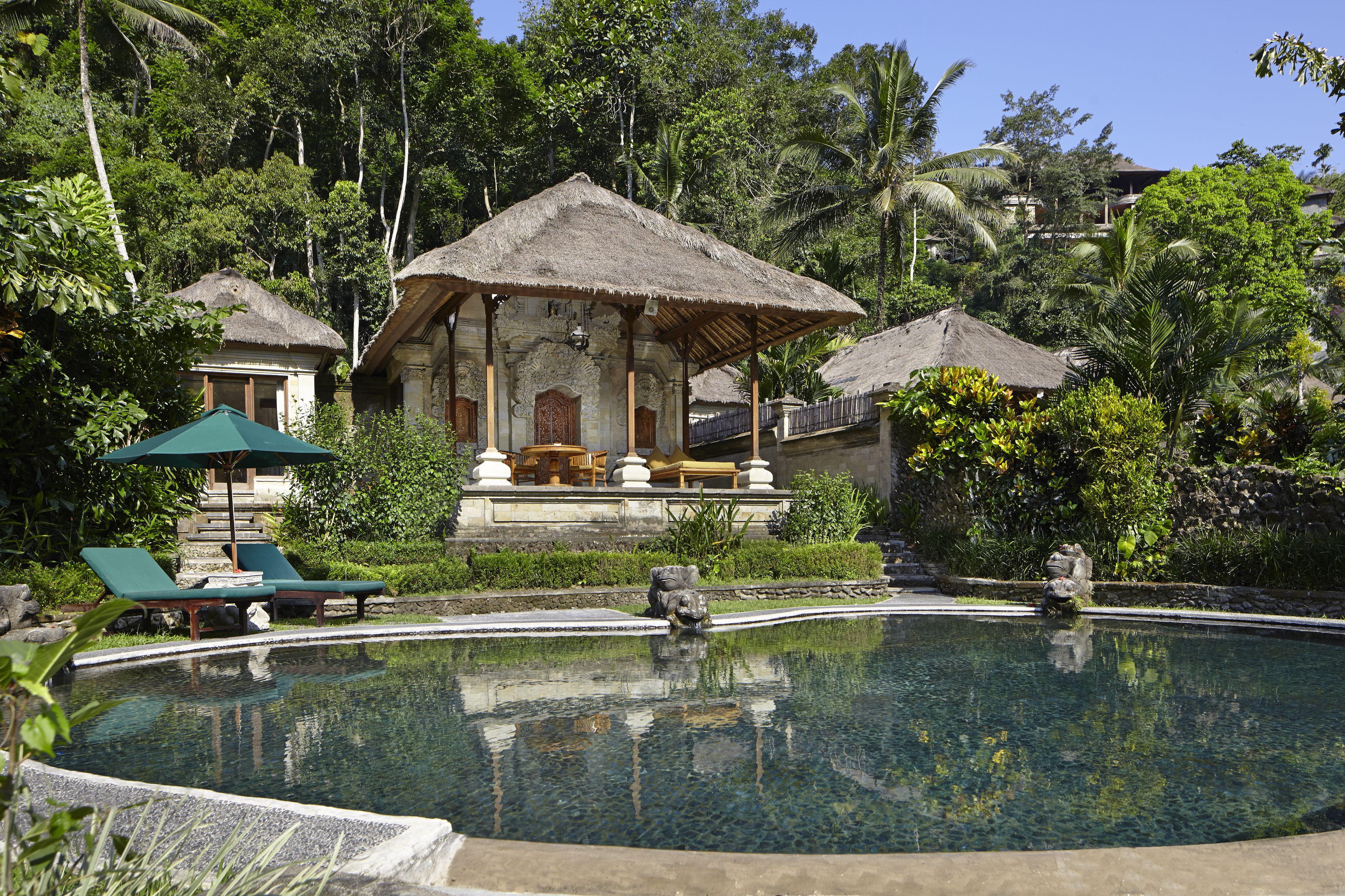 Un espace piscine avec des chaises longues et une structure dotée d’un toit de chaume.