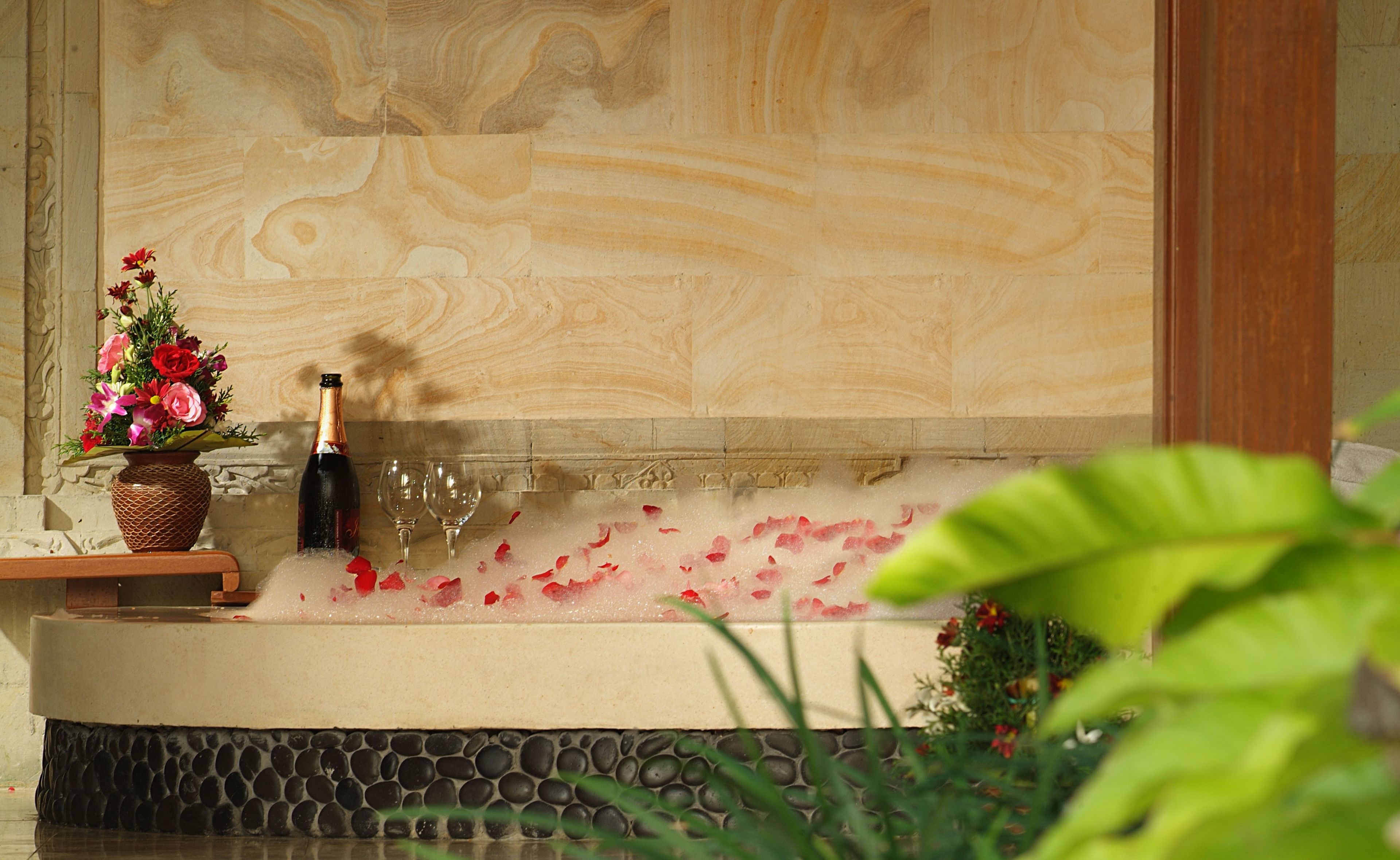 A spa area with a stone bathtub, a flower vase, and a bottle of champagne.