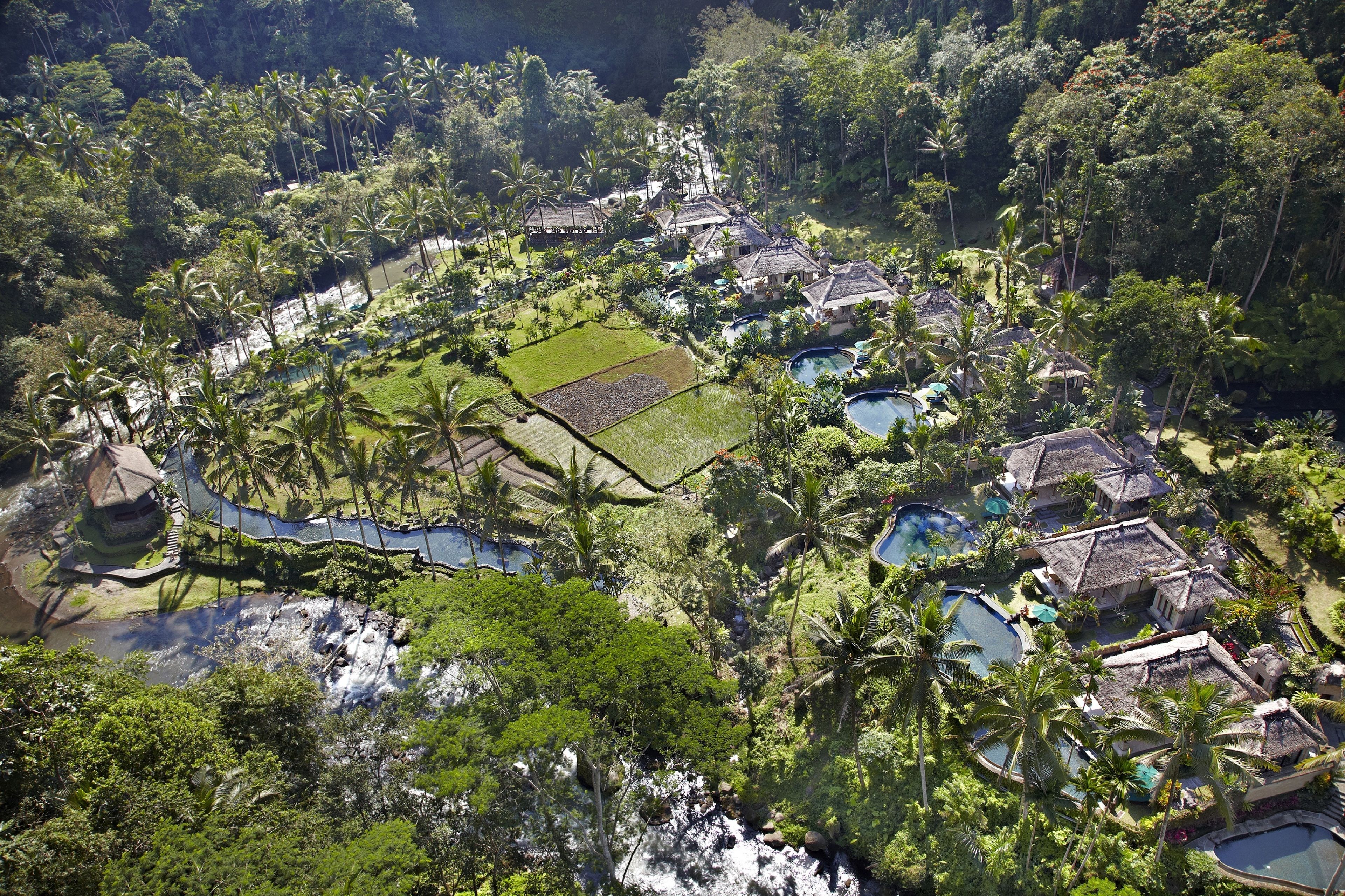 An aerial view of a resort with multiple pools, thatched-roof buildings, and lush greenery.