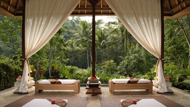 A serene outdoor spa area with two wicker beds, a central fire pit, and lush tropical foliage in the background. - Royal Pita Maha (Ubud)