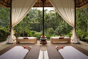 A serene outdoor spa area with two wicker beds, a central fire pit, and lush tropical foliage in the background. - Royal Pita Maha (Ubud)