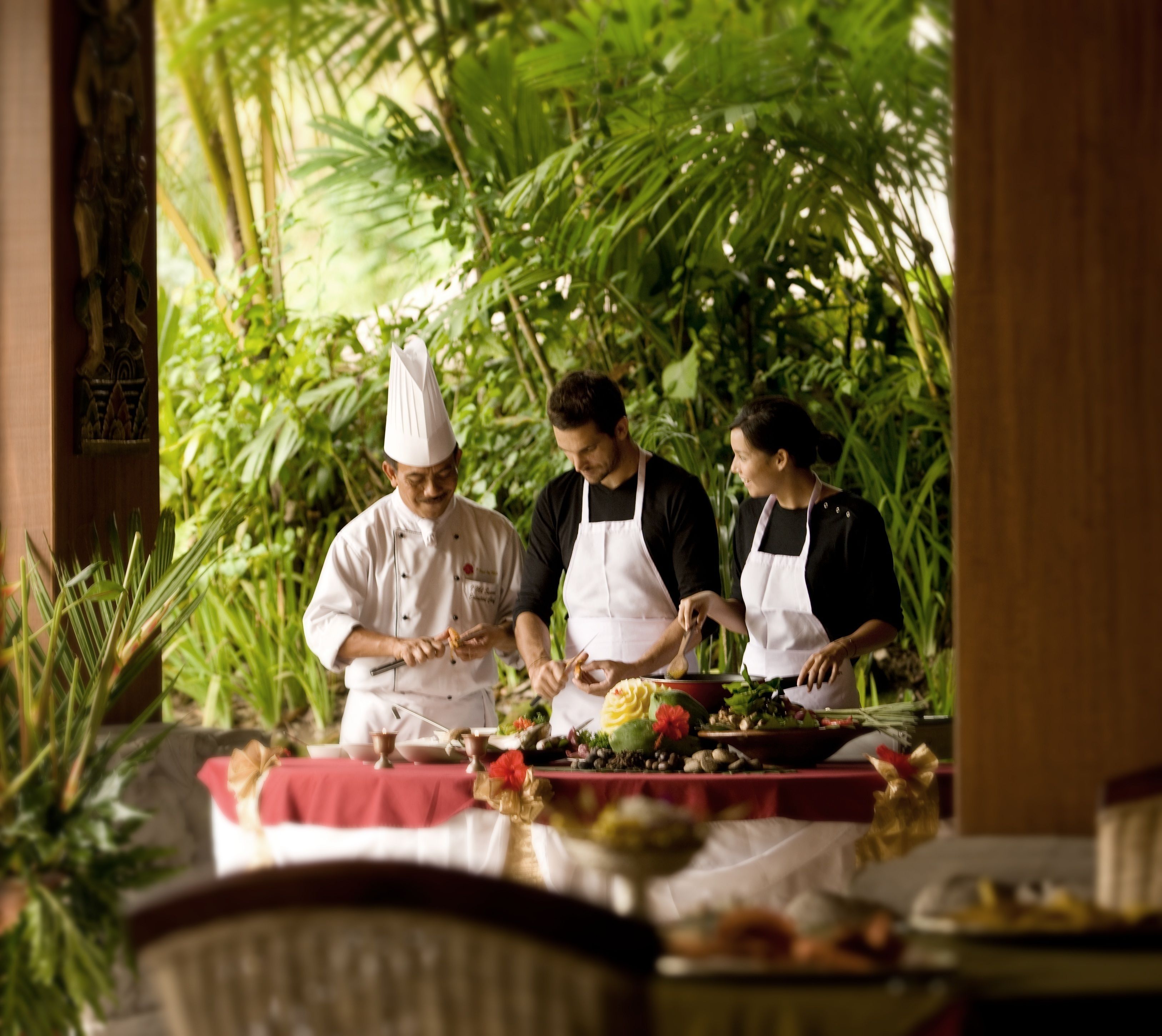 A chef preparing food outdoors with lush greenery in the background.