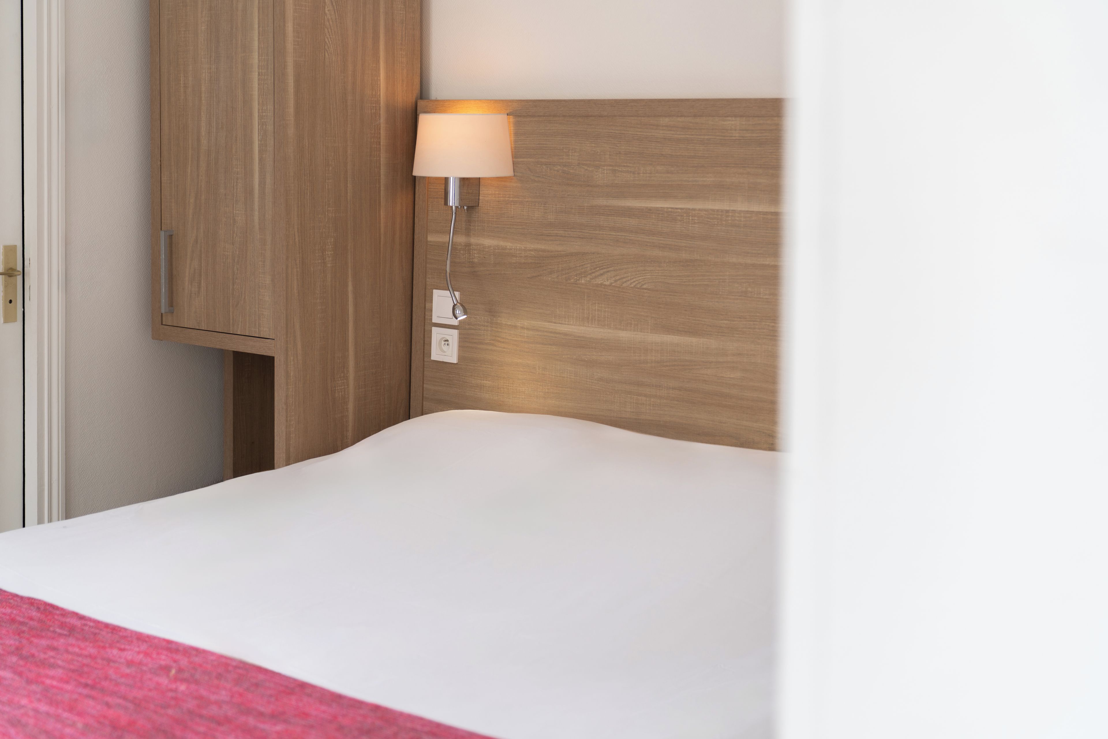 A hotel room with a wooden headboard, a bedside lamp, and a white bedspread.