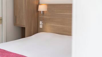 Een hotelkamer met een houten hoofdeinde, een bedlampje en een witte spreideken.