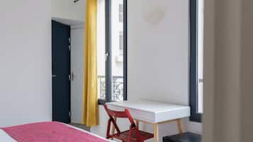 Una habitación con cama, escritorio, silla y ventana con cortinas.