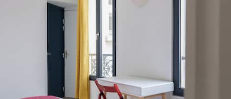 Una habitación con cama, escritorio, silla y ventana con cortinas.