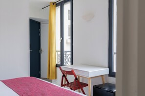 Een kamer met een bed, een bureau, een stoel en een raam met gordijnen.