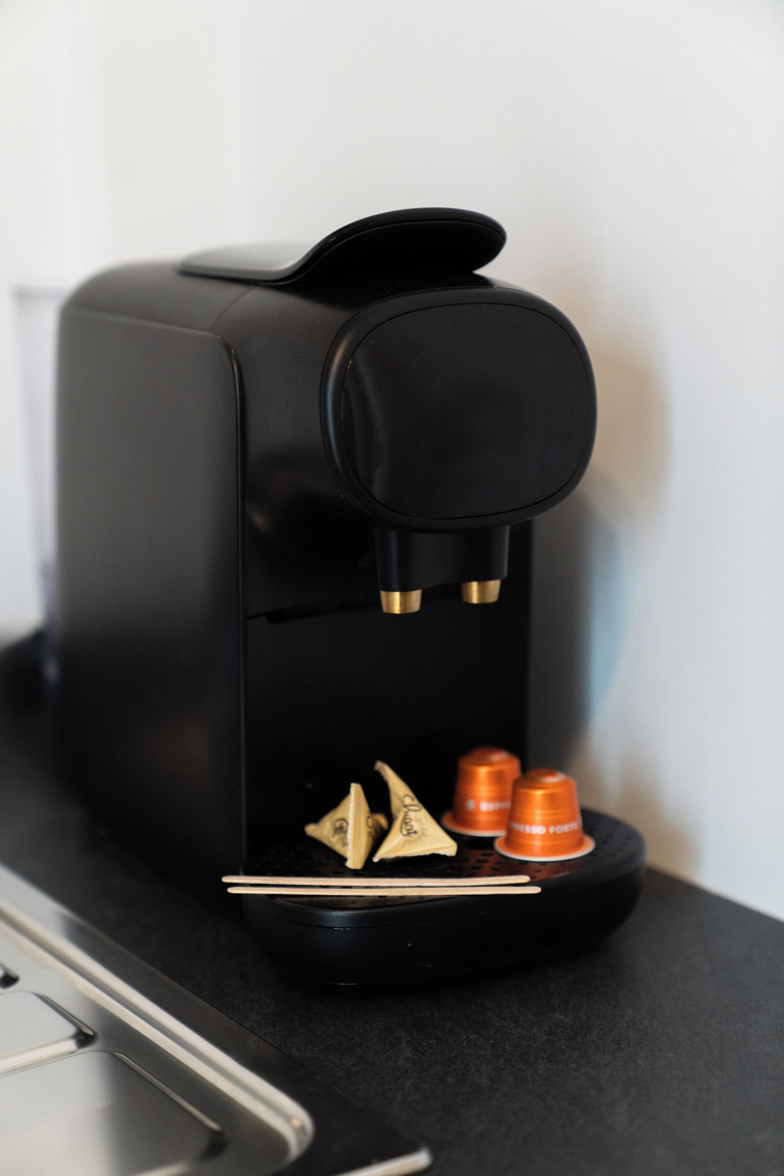 A black coffee machine with a single coffee pod and two orange capsules on a countertop.