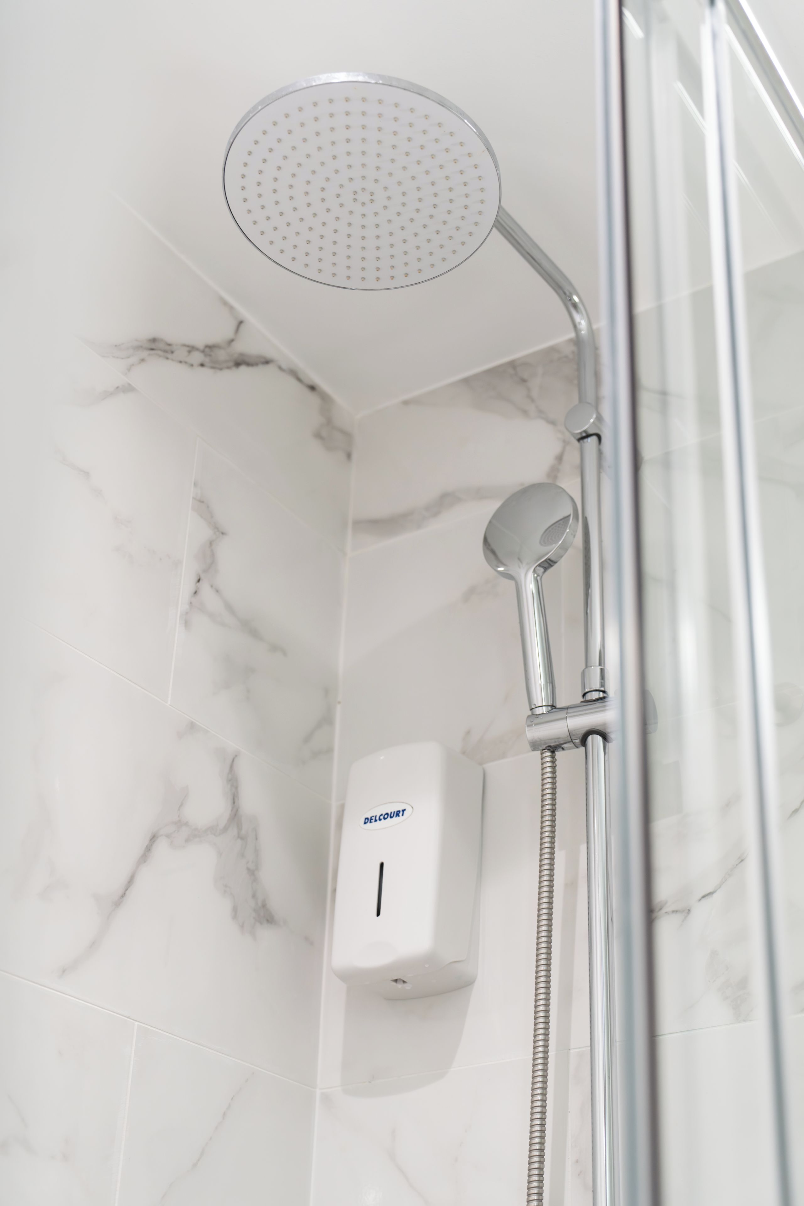 A shower with a handheld showerhead, a handheld showerhead, and a wall-mounted control panel.