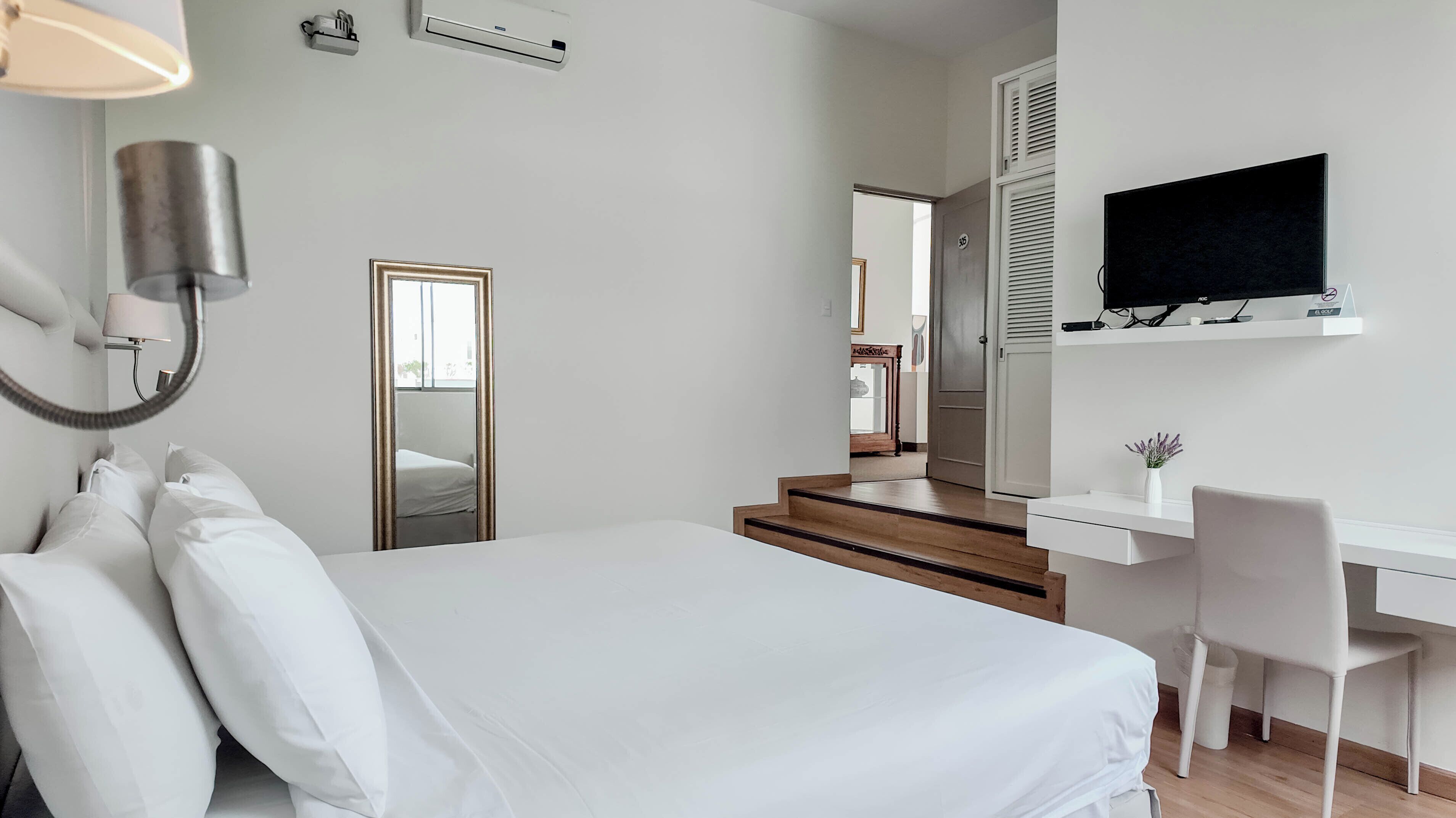 A bedroom with a bed, a desk, a chair, a TV, and a mirror.