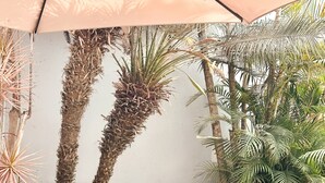 Un espacio al aire libre con mobiliario de mimbre, una mesa de vidrio y diversas plantas.