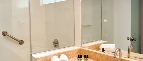 A modern bathroom with a glass shower enclosure, a large mirror, and a marble countertop with a sink and toiletries.