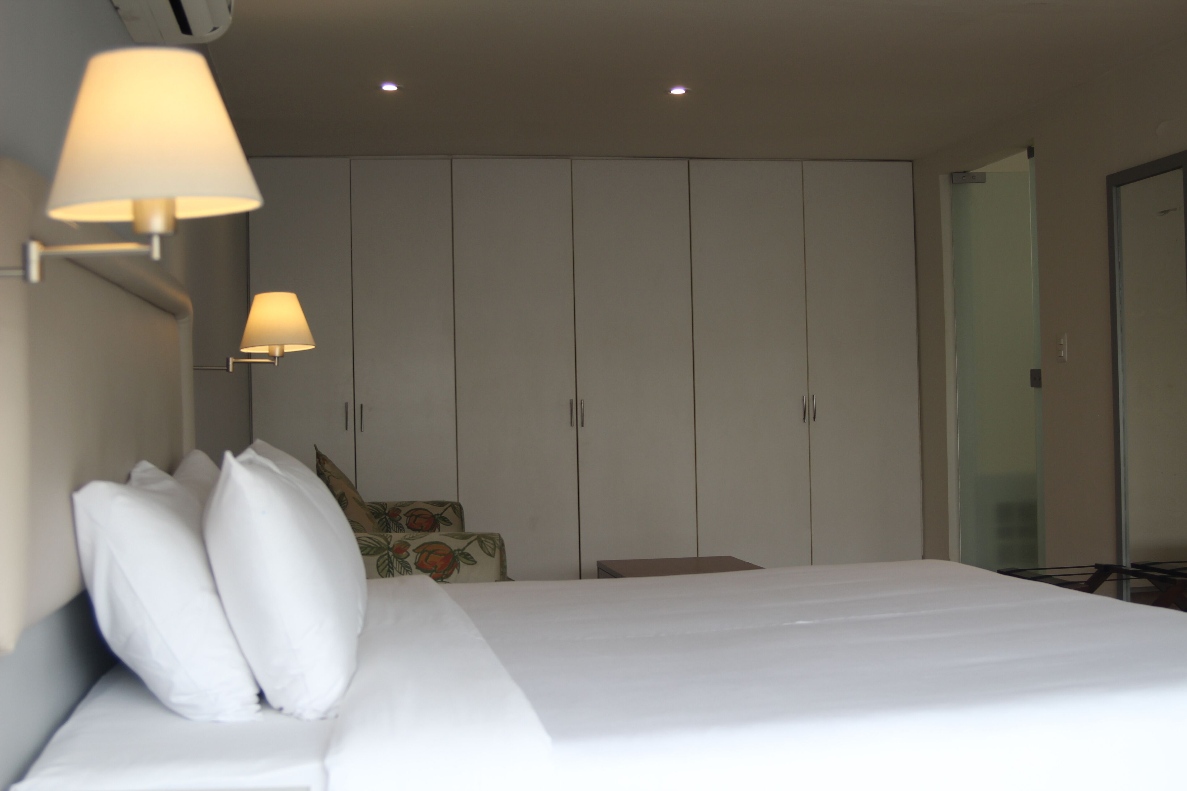 Una habitación de hotel con cama, un armario y dos lámparas fijadas a la pared.