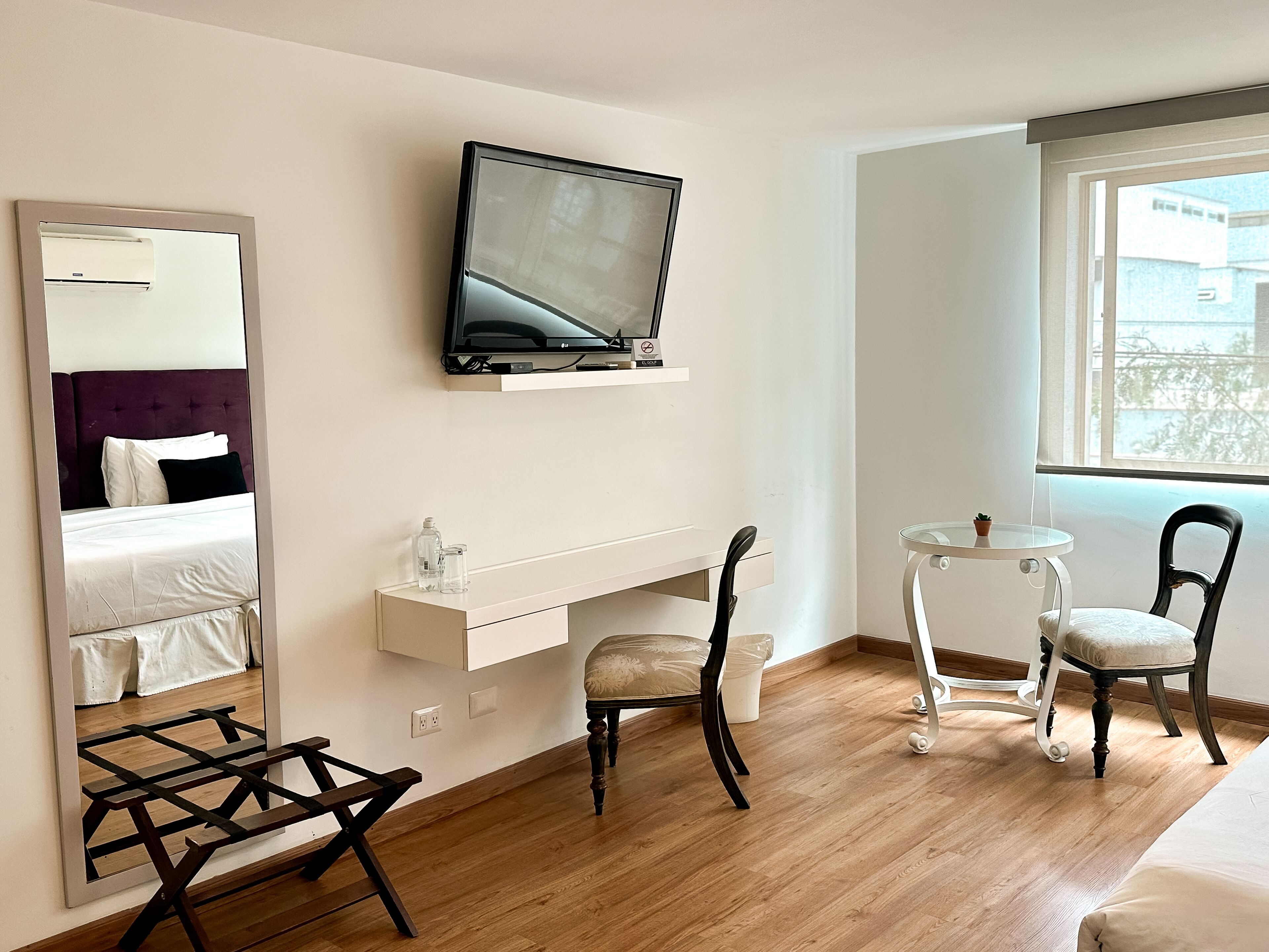 Een hotelkamer met een bed, een aan de muur bevestigde televisie, een bureau met stoel, en een raam met uitzicht.