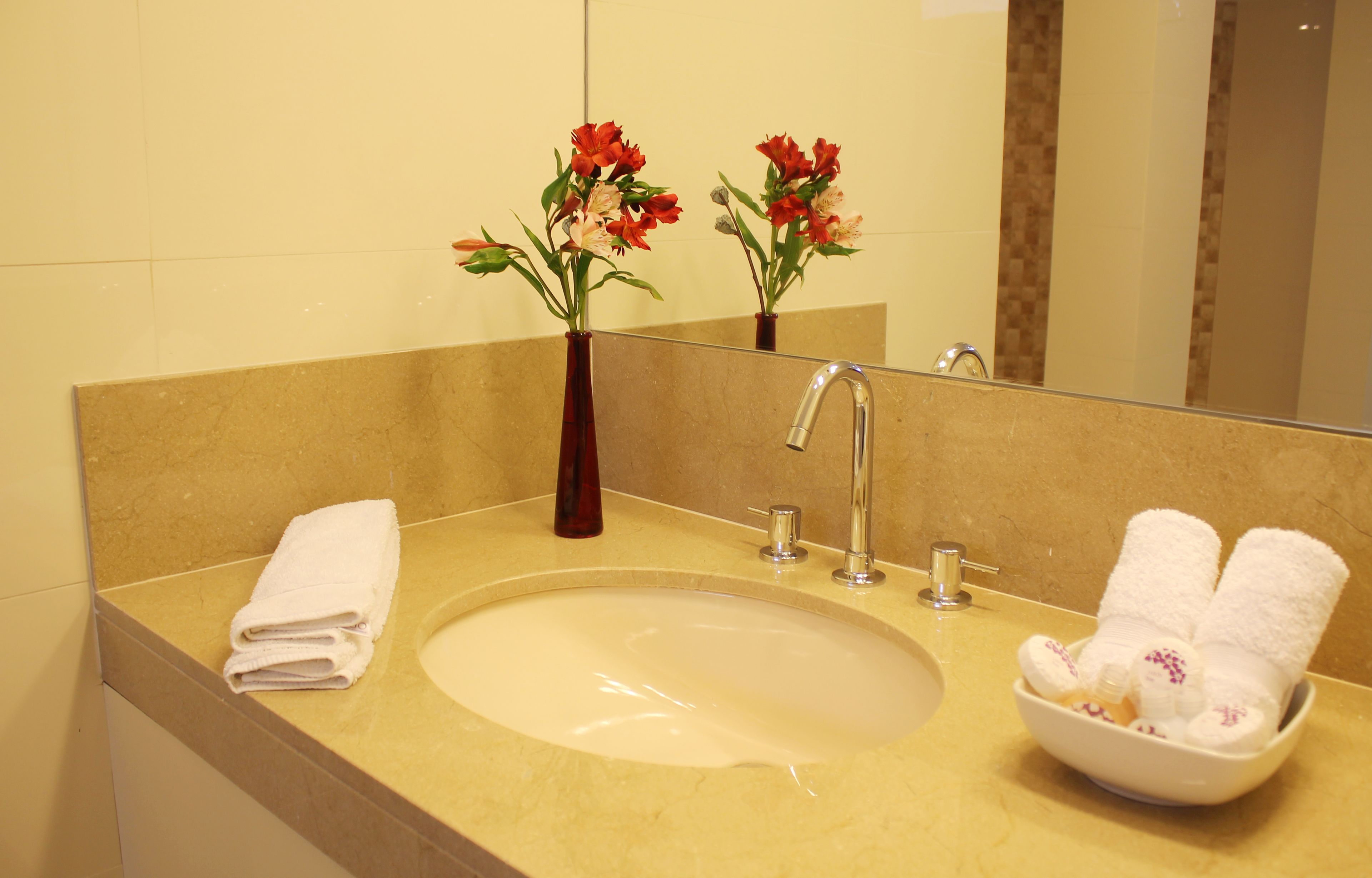 A bathroom with a beige sink, a mirror, and two flower arrangements in a vase.